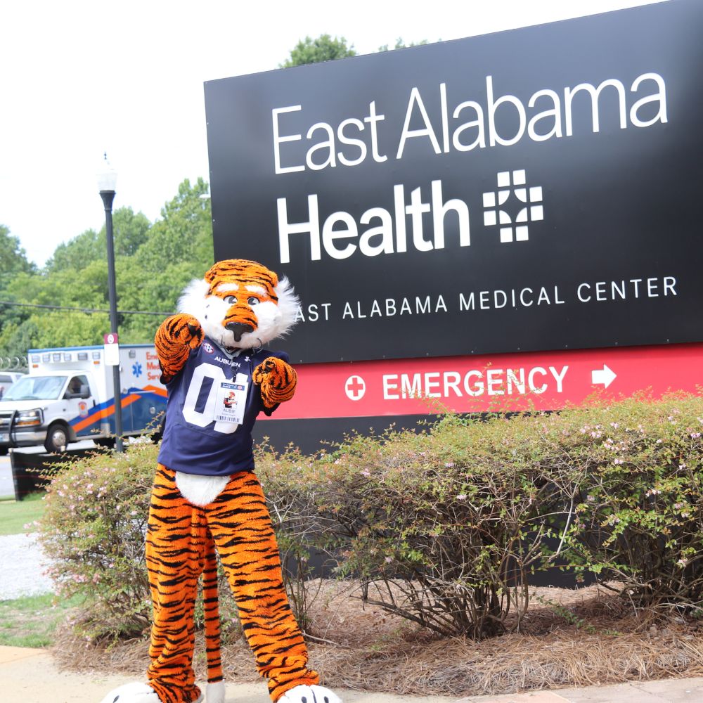 Aubie the Tiger in front of an East Alabama Health sign.